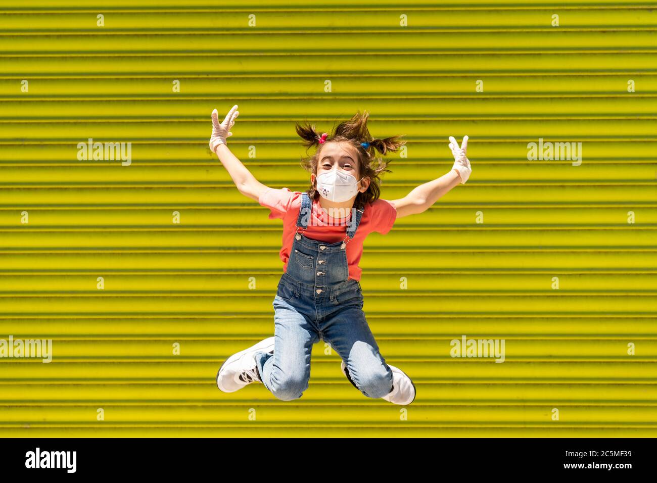 Bambina saltando indossando una maschera di protezione contro il coronavirus Foto Stock
