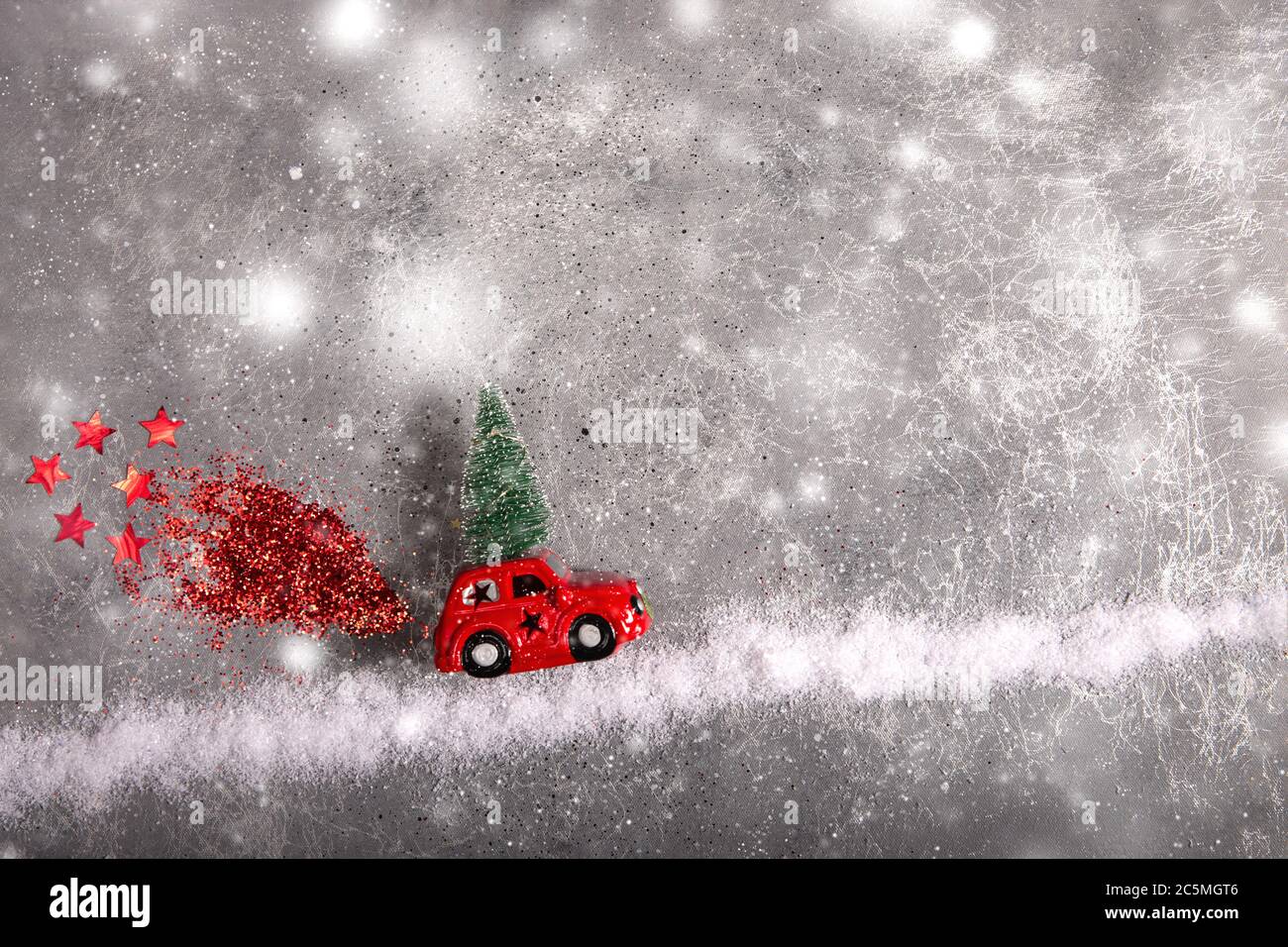 Giocattolo di Natale rosso auto con abete sul tetto su strada neve con rosso sequin fumo. Foto Stock