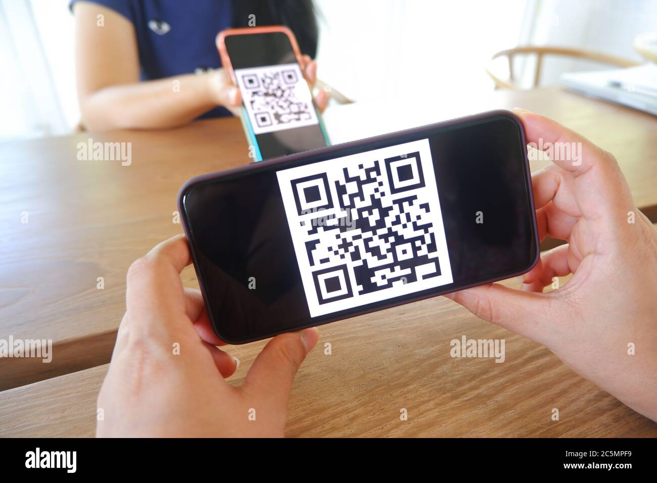 La mano delle donne utilizza un'applicazione per telefoni cellulari per eseguire la scansione dei codici QR nei negozi che accettano pagamenti digitali senza denaro e etichette di plastica sul tavolo. QR c Foto Stock