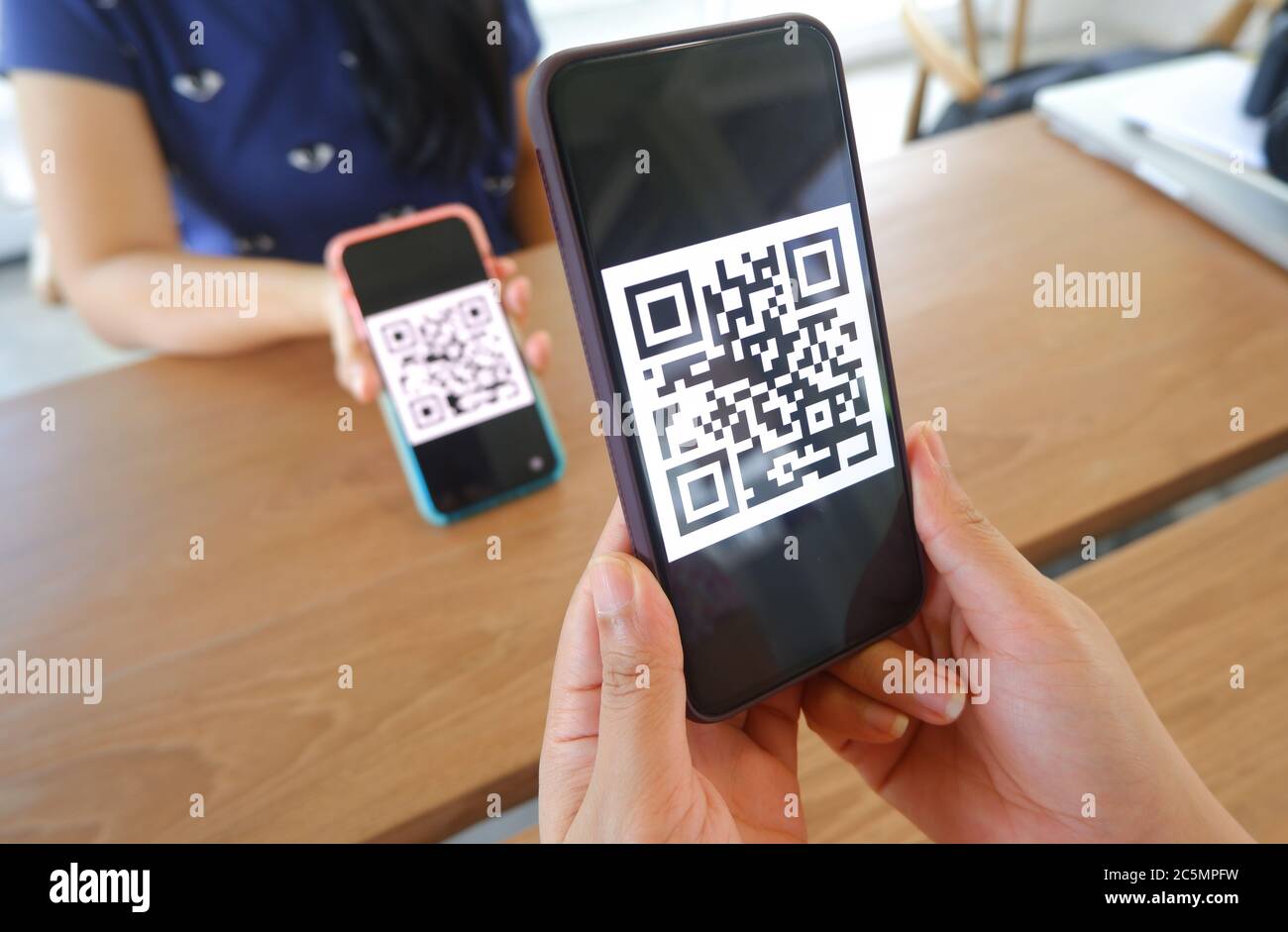 La mano delle donne utilizza un'applicazione per telefoni cellulari per eseguire la scansione dei codici QR nei negozi che accettano pagamenti digitali senza denaro e etichette di plastica sul tavolo. QR c Foto Stock