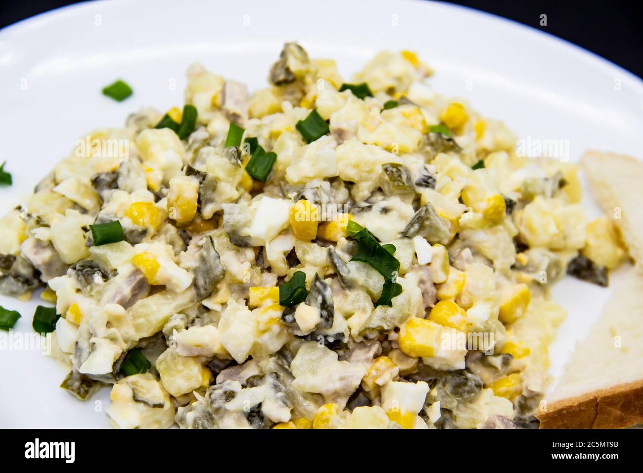 Insalata Ucraina e russa Olivier secondo una nuova ricetta su un piatto bianco. Insalata sana Olivier con carne, mais e fette di pane bianco. DELIC Foto Stock