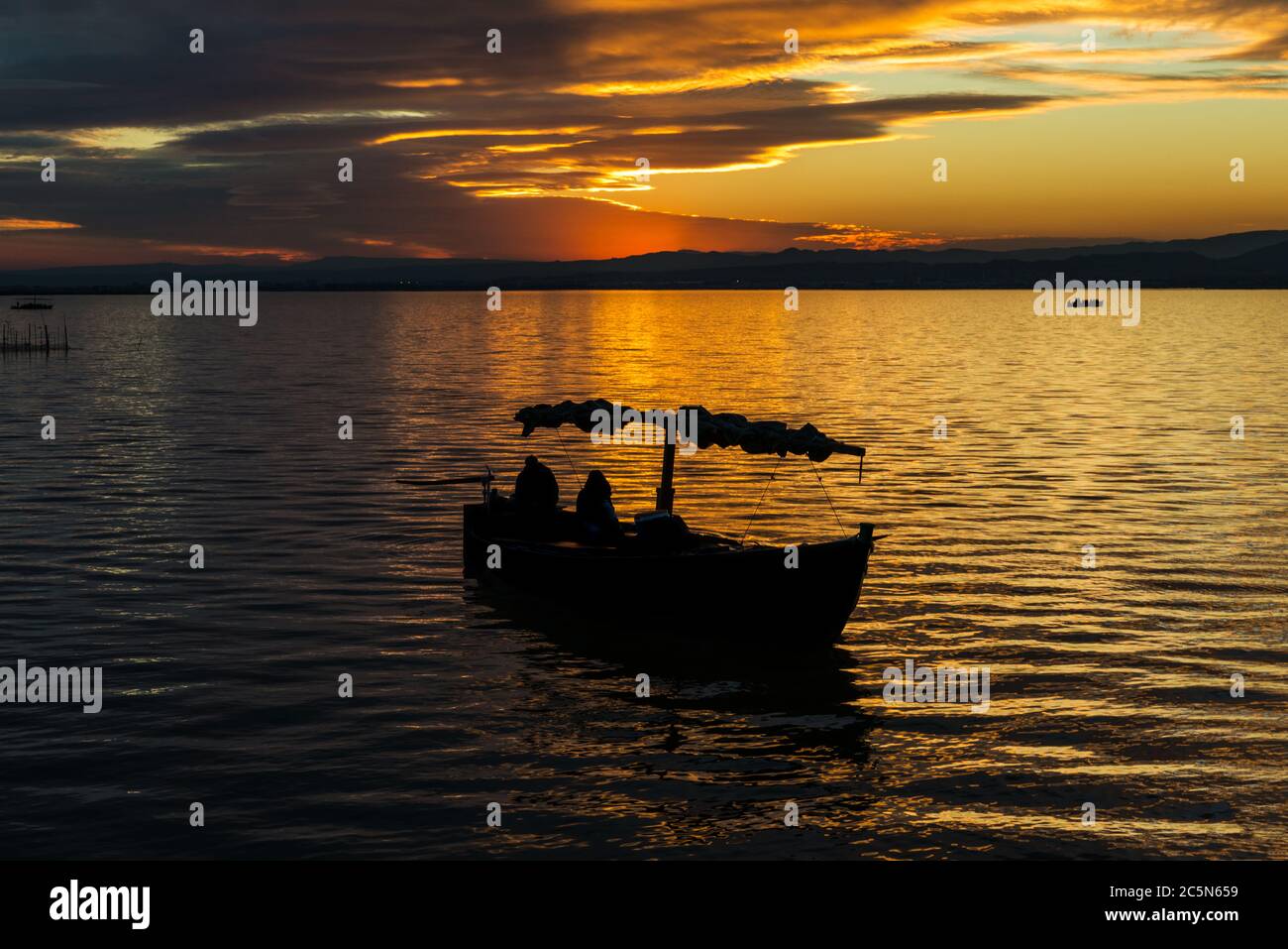 Silhouette di una piccola barca tradizionale al tramonto nell'Albufera a Valencia, una laguna d'acqua dolce e un estuario nella Spagna orientale. Foto Stock