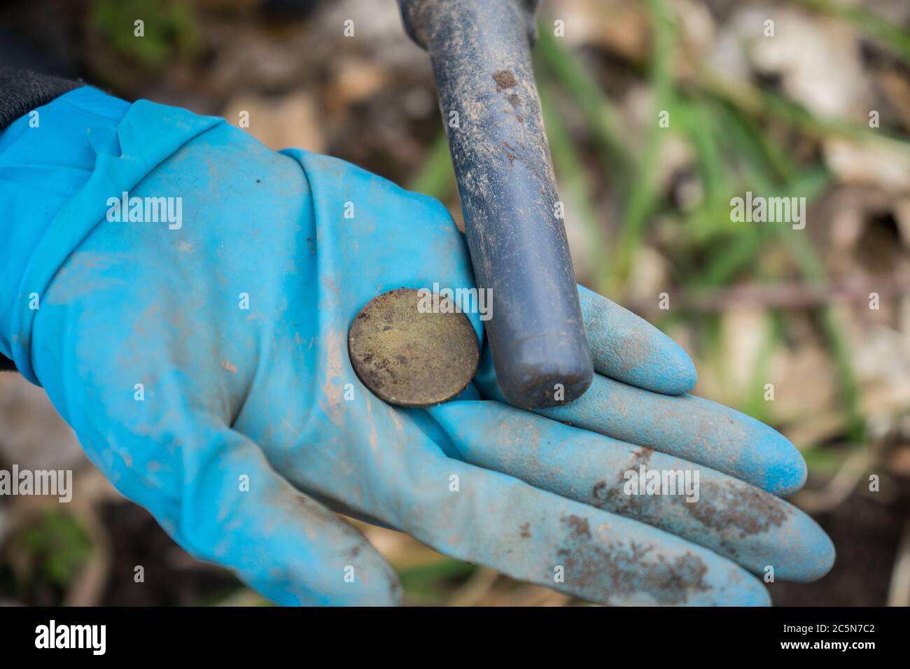 Trovata vecchia moneta preziosa in mano archeologa con pinpointer metal detector. Foto Stock