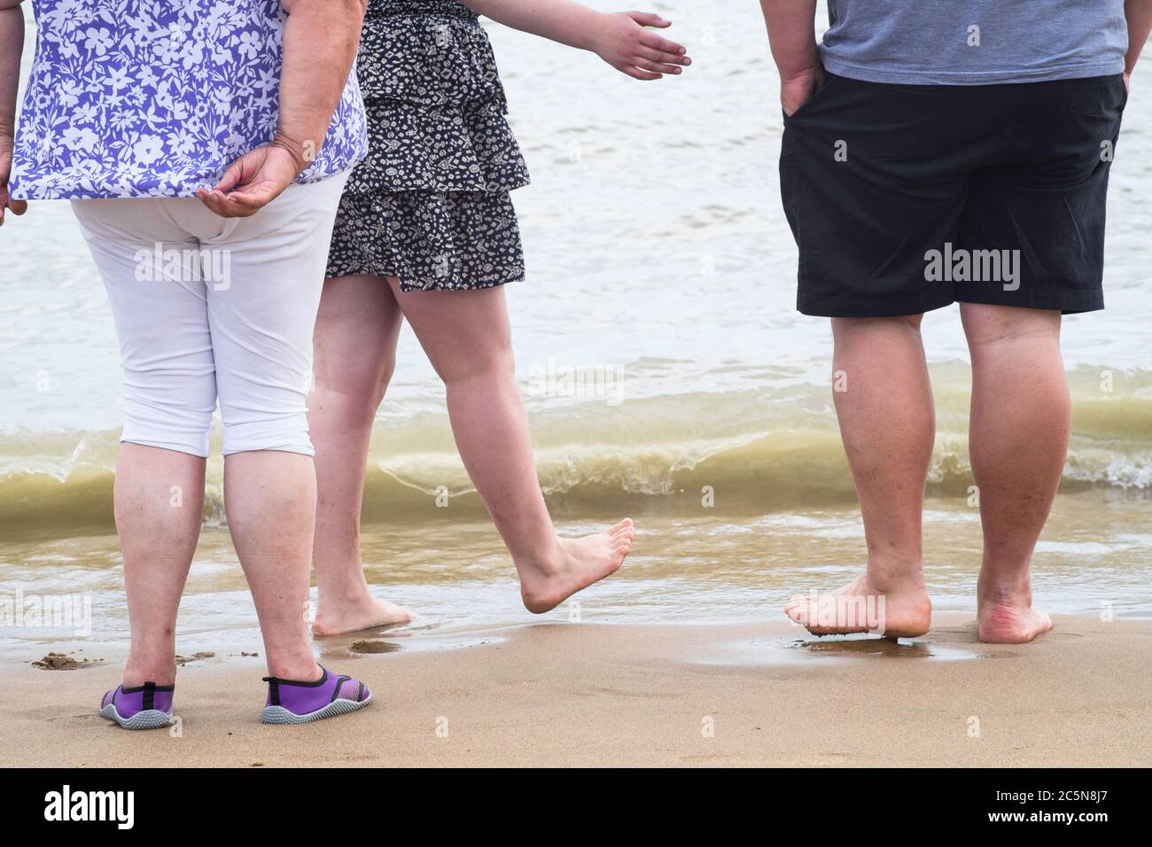 Tre persone molto grasse, donne e un uomo, a piedi nudi sulla spiaggia di Broadstairs. Solo il corpo inferiore è visibile Foto Stock