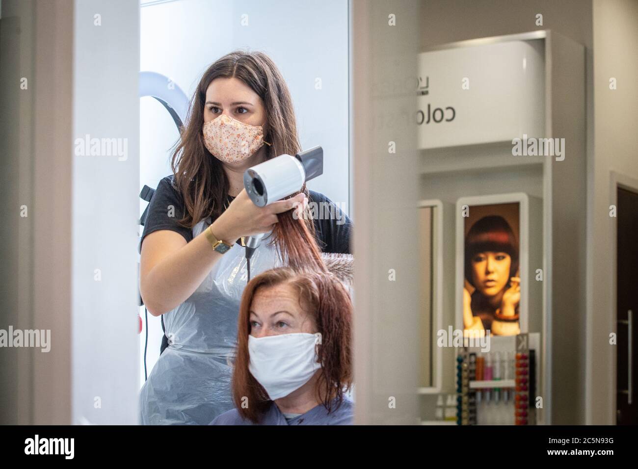 Parrucchiere indossando maschera mentre lavora e tagliando i capelli in parrucchiere come il coronavirus lockdown eases in Inghilterra 4 luglio 2020 Foto Stock