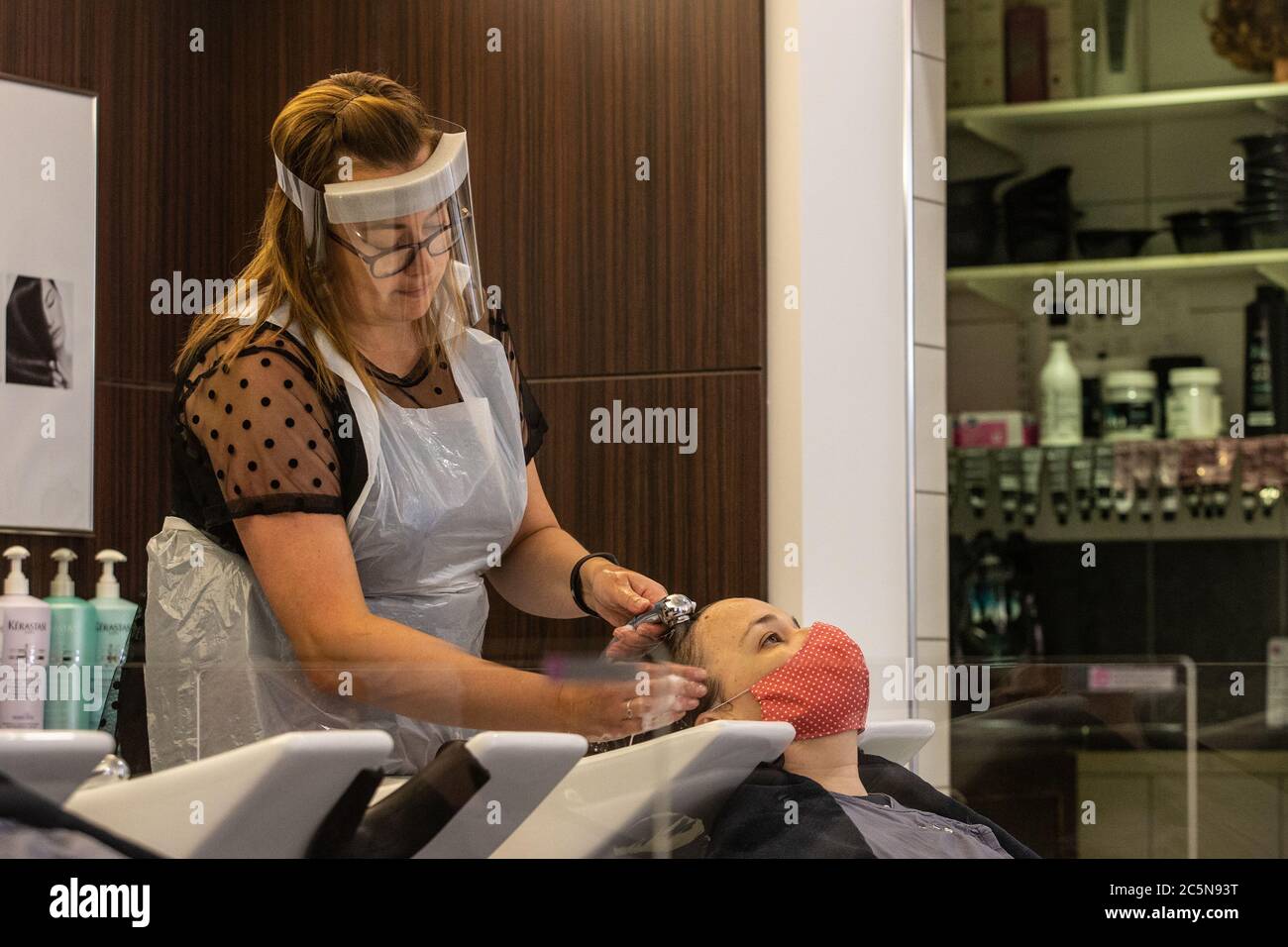 Parrucchiere indossando DPI visiera viso lavaggio capelli di cliente indossare maschera viso in parrucchiere durante i primi giorni di blocco alleggerimento in Inghilterra 2020 Foto Stock