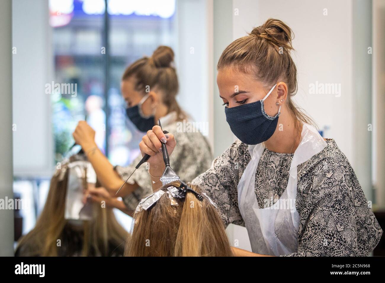 Parrucchiere indossando maschera mentre lavora e tagliando i capelli in parrucchiere come il coronavirus lockdown eases in Inghilterra 4 luglio 2020 Foto Stock