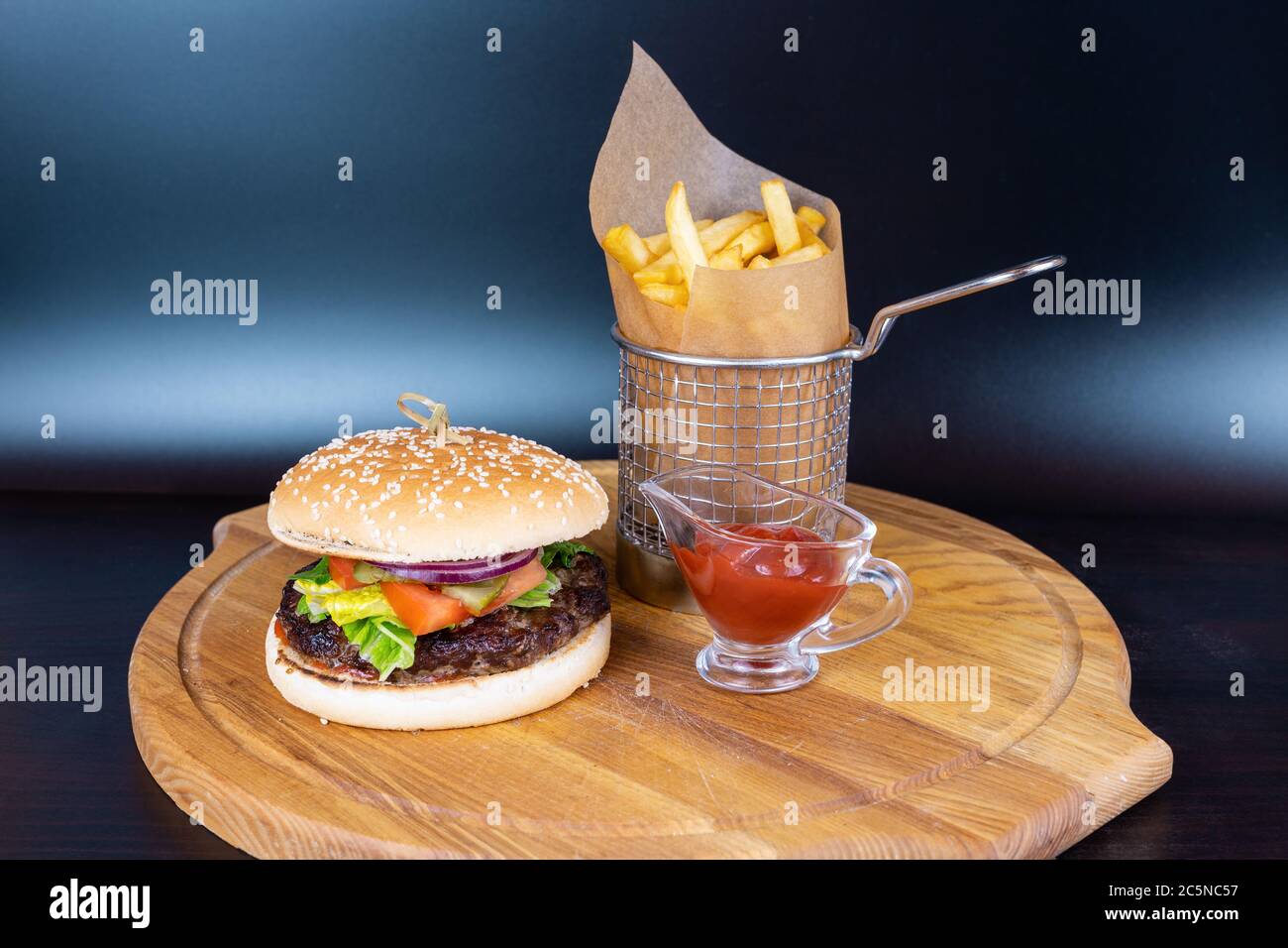 Hamburger fresco e patate fritte con salsa rossa su tavola di legno su fondo blu intenso Foto Stock