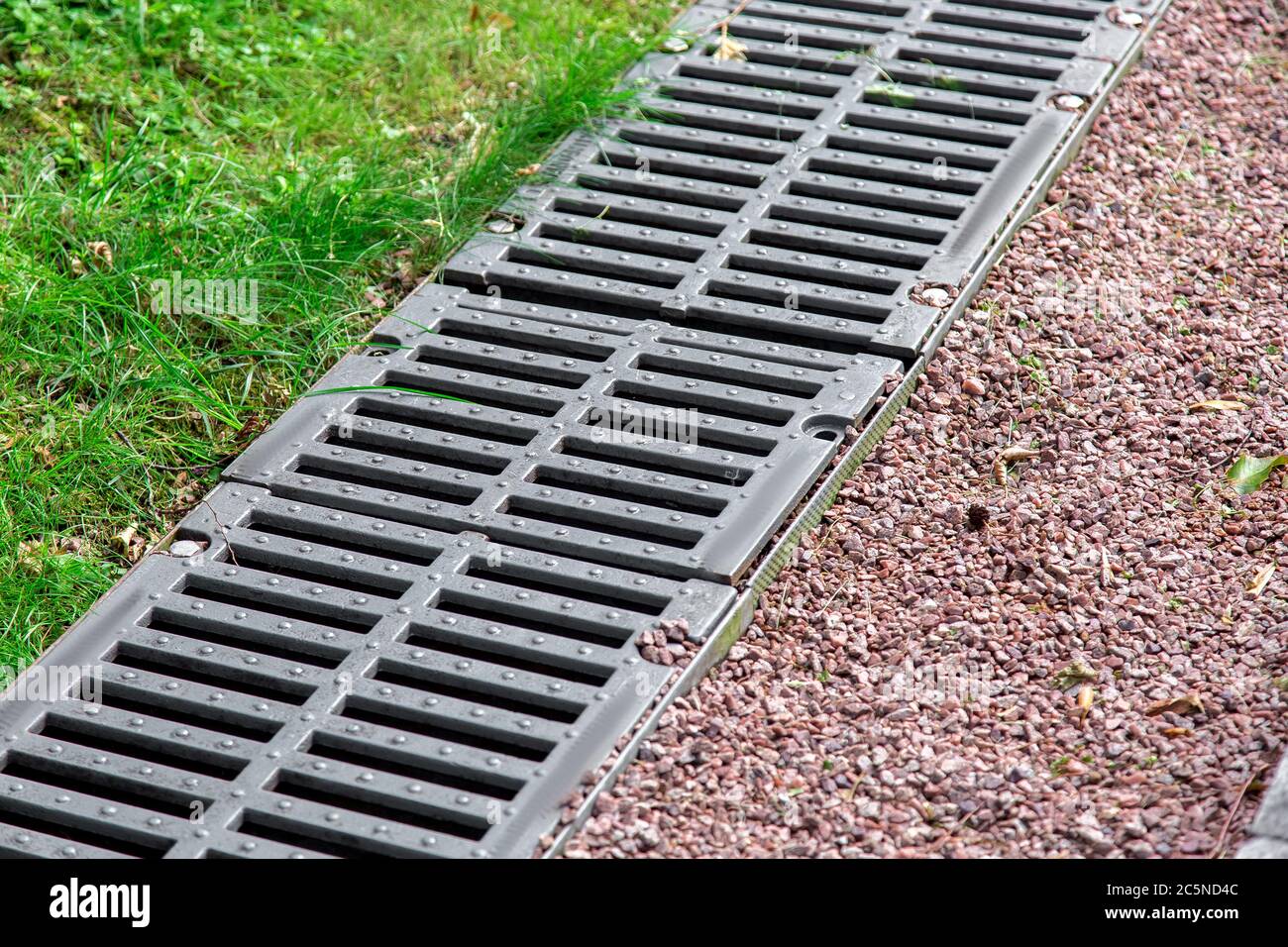 grata di ferro di un canale di drenaggio su un paesaggio con ciottoli e erba verde, dettaglio closeup. Foto Stock