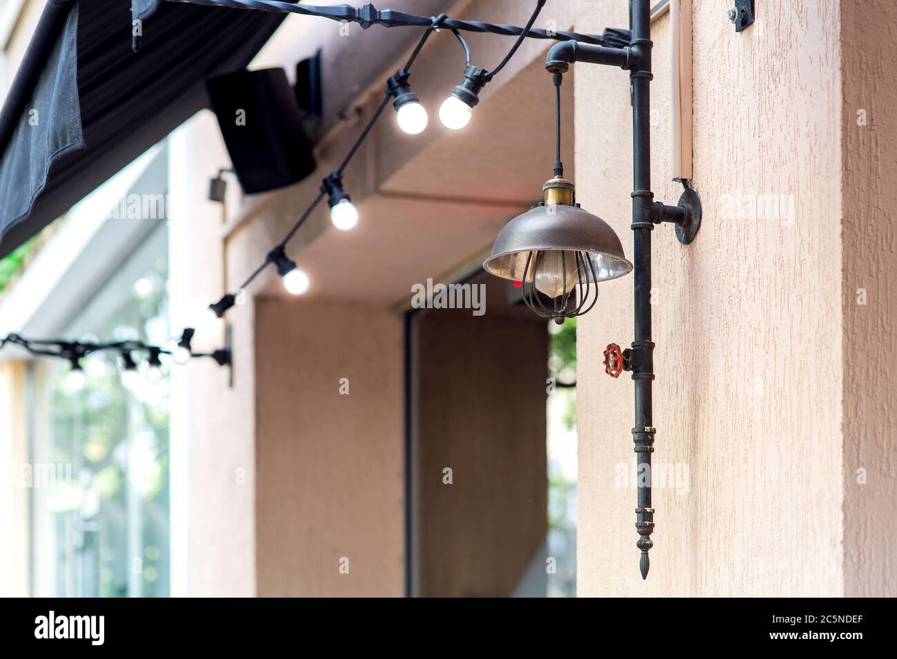 lampada da strada in stile loft sulla parete della facciata dell'edificio con un ghirlaio di lampadine e un baldacchino sopra la finestra. Foto Stock