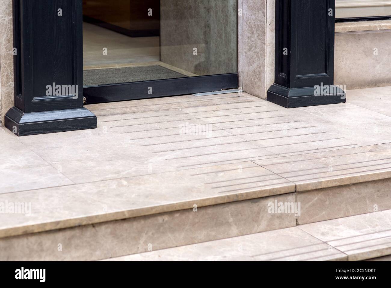 una soglia con un gradino da una piastrella di marmo, un ingresso al  negozio con una porta di vetro e colonne di legno di una facciata  dell'edificio Foto stock - Alamy