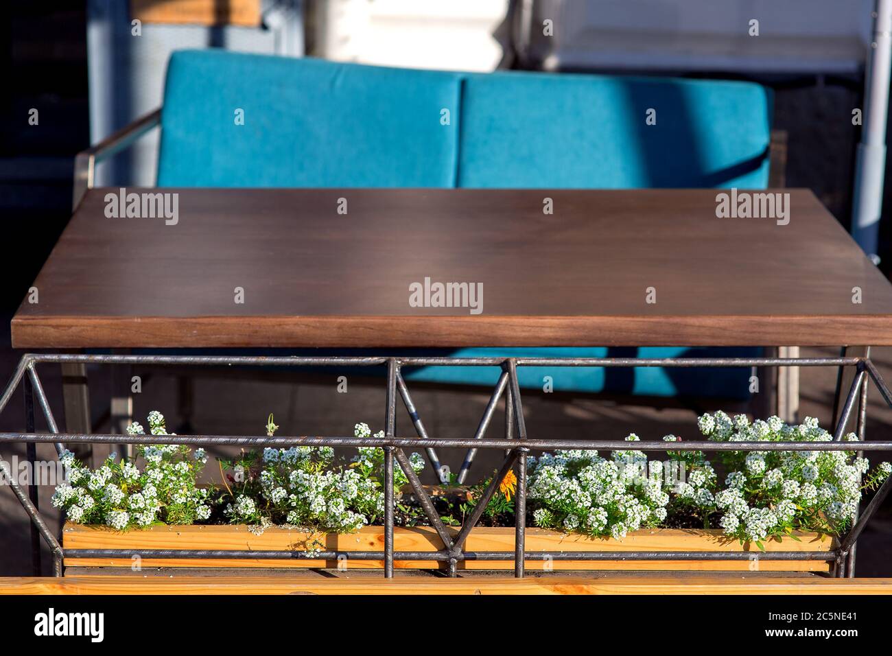 Vaso di design realizzato in ferro tubolare cornice con fiori verdi e fiori bianchi al tavolo di legno marrone con sedia blu di un caffè all'aperto, clos Foto Stock