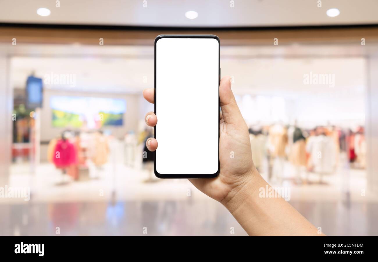 Telefono cellulare bianco mockup. Smartphone con mano e sfondo sfocato del negozio di abbigliamento per il testo o l'illustrazione della pubblicità. Foto Stock