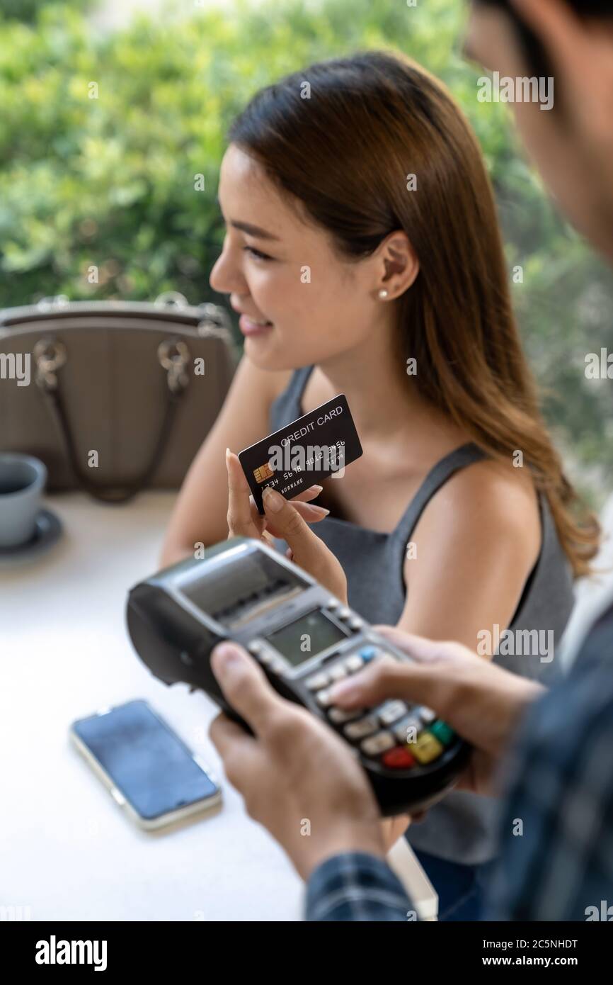 Donna asiatica cliente tenere contactless carta di credito per effettuare il pagamento online dopo aver mangiato in nuovo normale ristorante distanza sociale. Contatto online Foto Stock