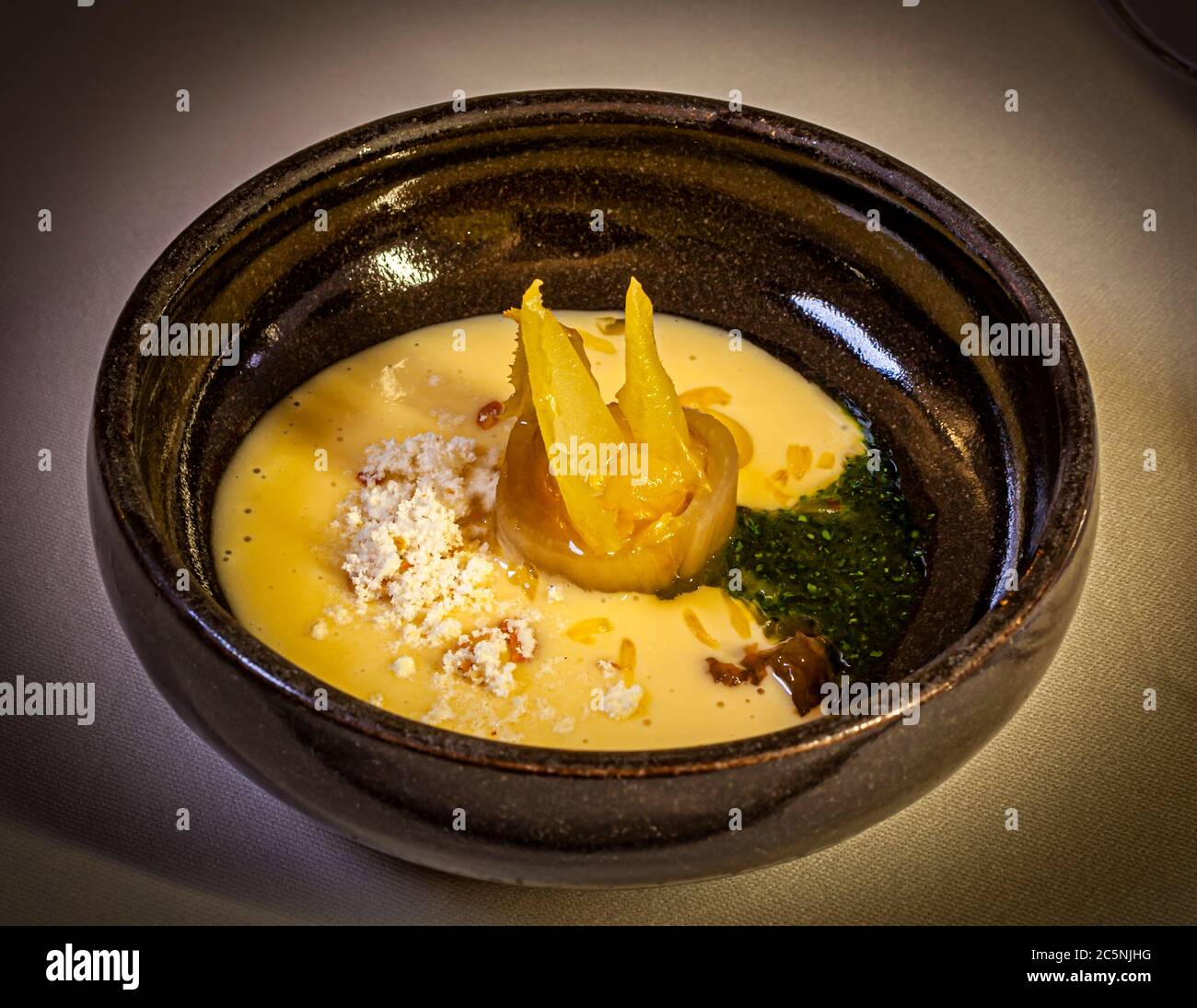 Un pezzo di mela glassato si adagia in una zuppa cremosa, guarnito con due sottili chips di mela, una salsa alle erbe verde scuro e un crumble croccante. Lo chef stellato Michelin Thomas Kellermann serve il piatto al ristorante gastronomico "Kastell" al castello di Wernberg, Wernberg-Köblitz, Alto Palatinato, Germania, nell'ambito di un menu di degustazione a più portate. Foto Stock