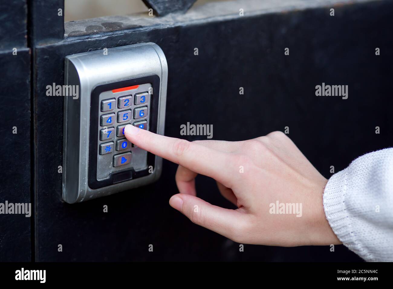 la mano femmina compone il codice di accesso sulla serratura elettronica premendo un dito con una retroilluminazione blu, avvicinando la serratura di sicurezza con la mano. Foto Stock