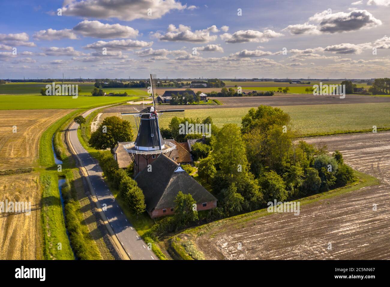 Veduta aerea di un piccolo borgo olandese con un mulino a vento in legno storico nel paesaggio agricolo della campagna, Groningen, Olanda. Foto Stock