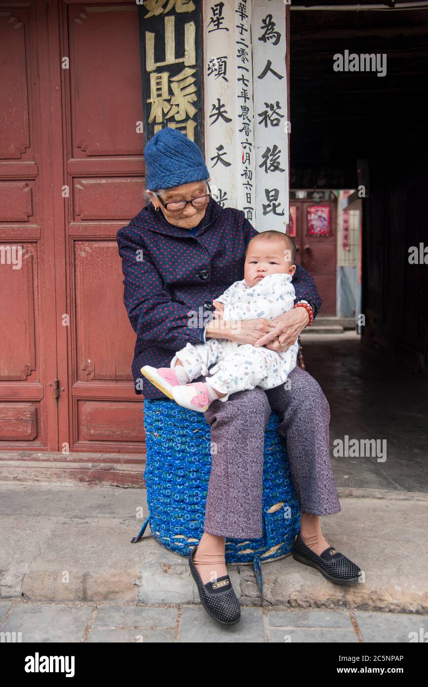 Vecchia nonna cinese seduta giù e tenendo la nipote del bambino nella sua città natale Dali, Cina del sud-ovest. Foto Stock