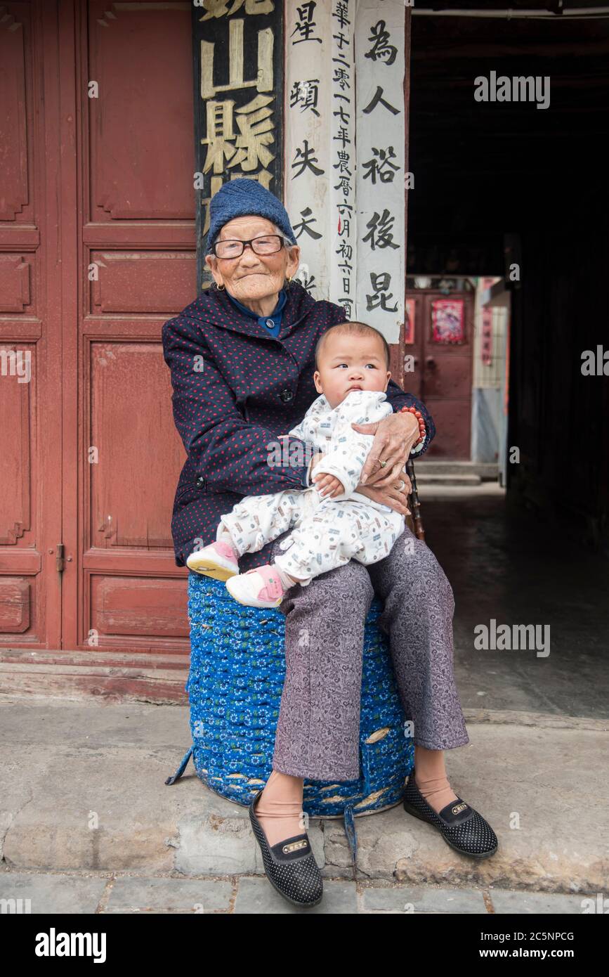 Vecchia nonna cinese seduta giù e tenendo la nipote del bambino nella sua città natale Dali, Cina del sud-ovest. Foto Stock