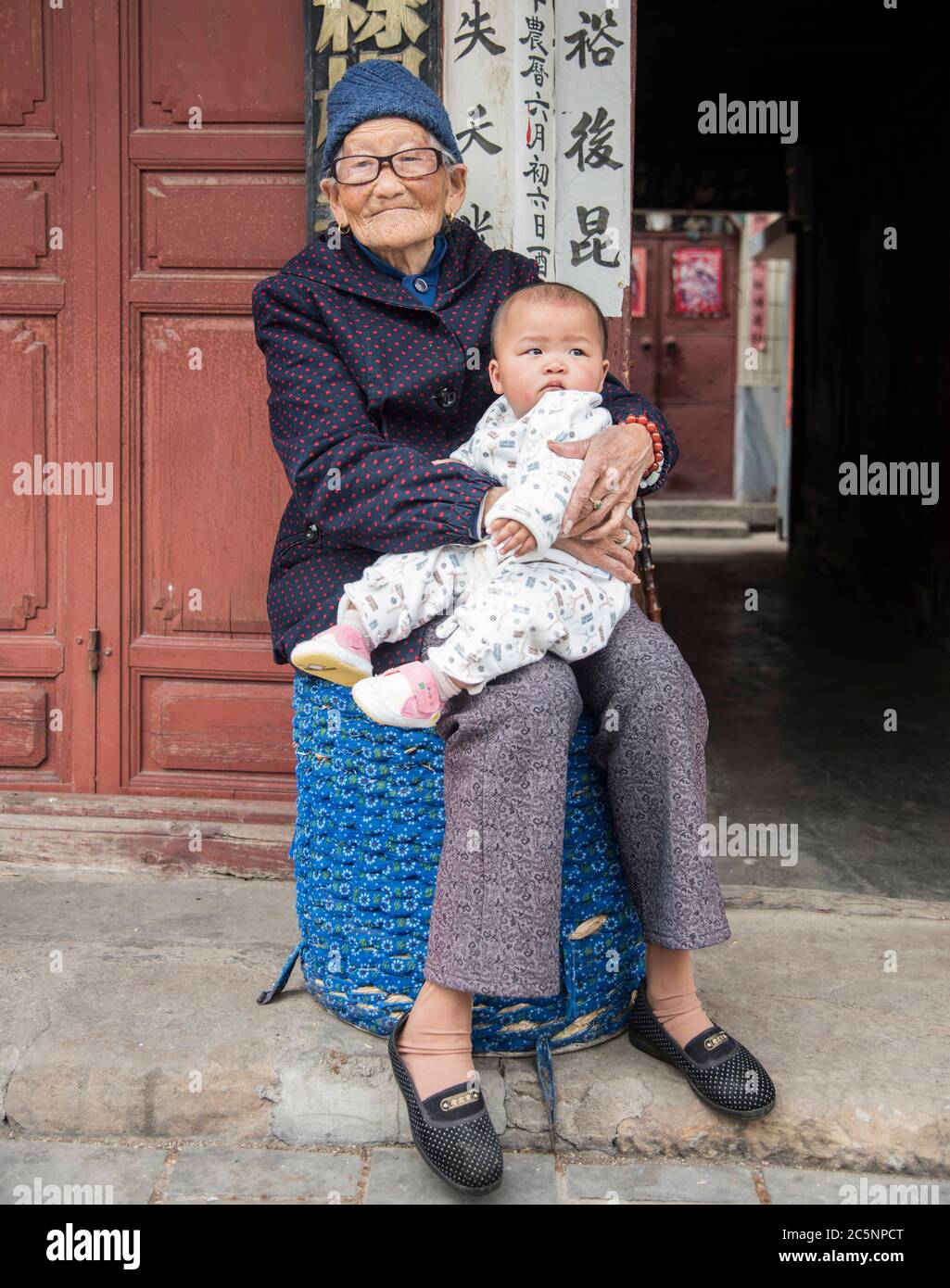 Vecchia nonna cinese seduta giù e tenendo la nipote del bambino nella sua città natale Dali, Cina del sud-ovest. Foto Stock