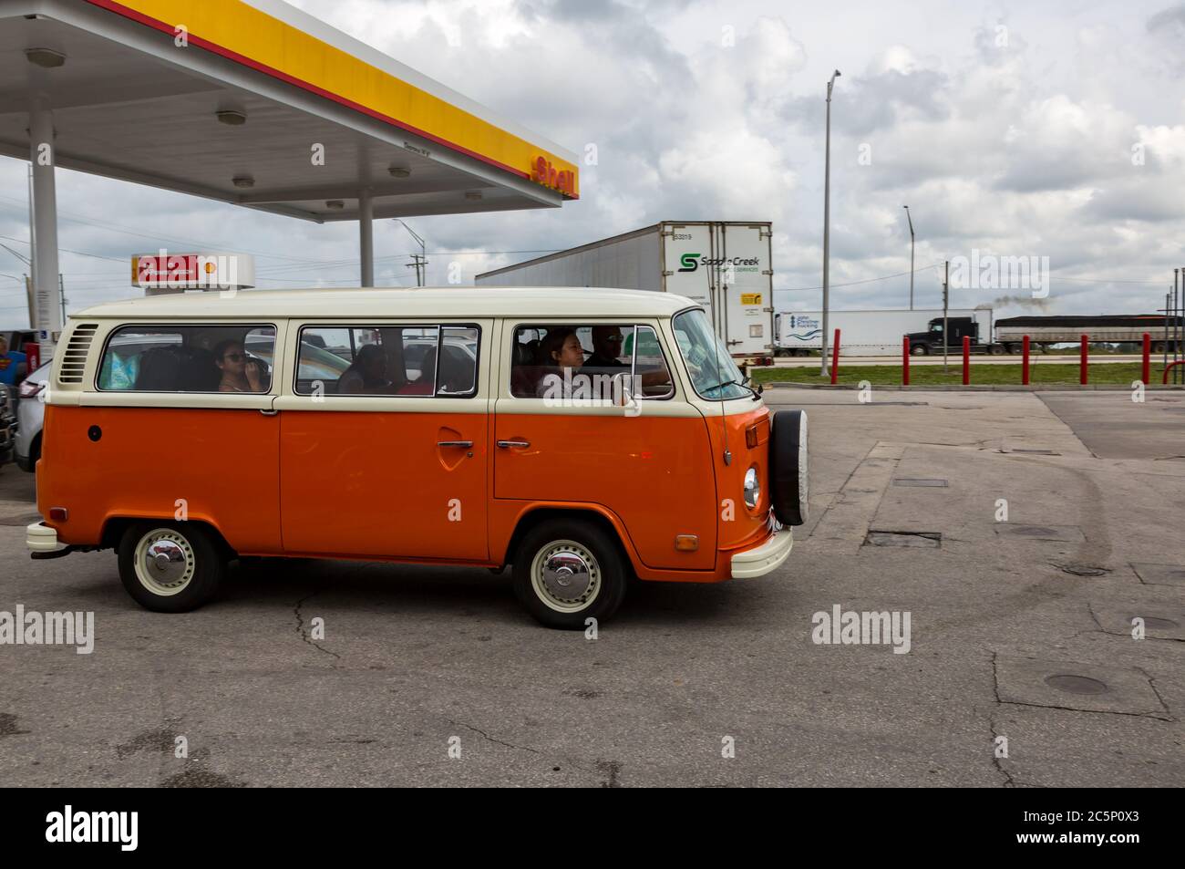 Un trasportatore arancione vintage Volkswagen Bus T2b parte dopo aver effettuato il rifornimento presso una stazione di servizio Lake Placid, Florida Shell. Foto Stock