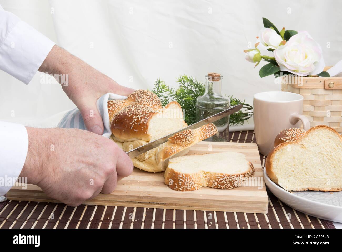 un panettiere taglia una fetta di un filone intrecciato di pane all'uovo di sesamo su un tagliere di legno Foto Stock