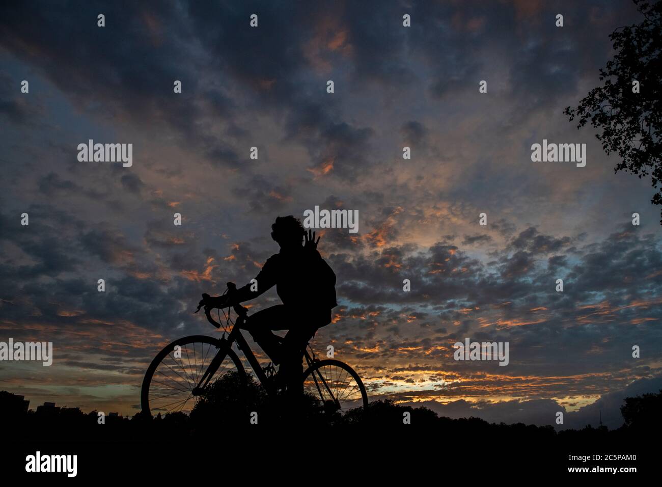 Un ragazzo si ondeggia dalla sua bicicletta mentre si pedala in un parco di Londra sotto un tramonto spettacolare Foto Stock