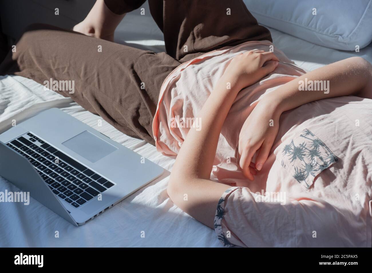 Procrastinazione, riposo dal lavoro: Una donna si appoggia a letto accanto ad un computer. Concetto di lavoro remoto, non essere in grado di essere produttivo, essere pigro lavoro Foto Stock
