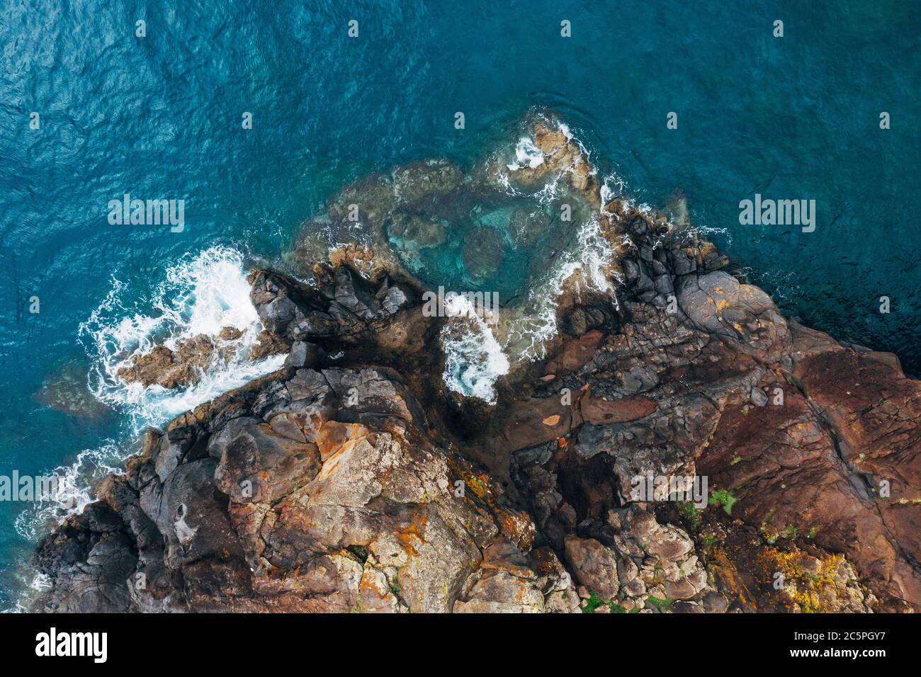 Vista aerea dall'alto delle onde turchesi dell'oceano Atlantico che si infrangono sulle rocce sulla riva portoghese dell'isola di Madera. Foto Stock