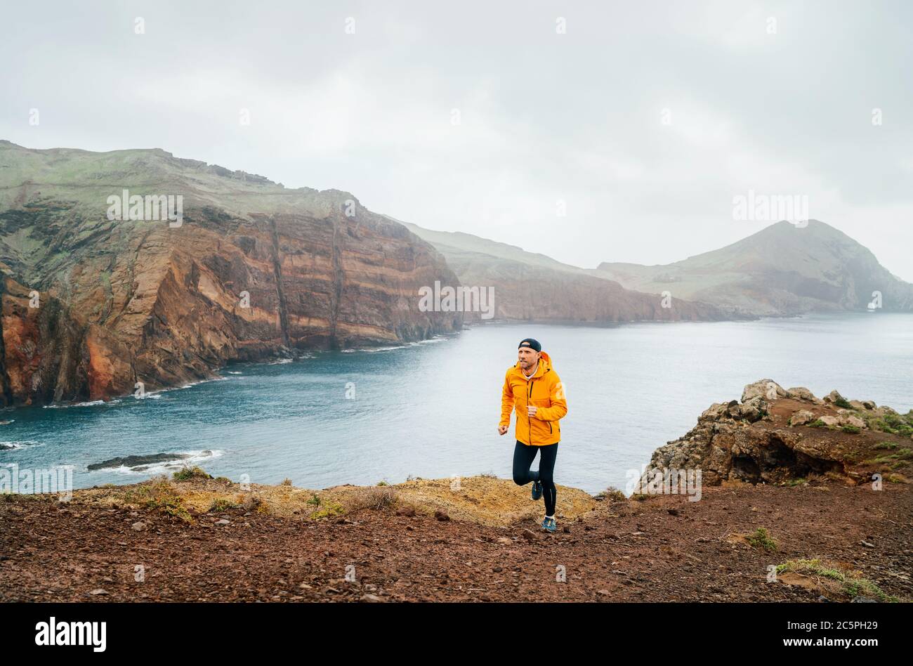 Trail runner uomo vestito arancione impermeabile giacca, running tights e scarpe jogging da Atlantic Ocean Bay gamma sulla penisola Ponta de Sao Lourenço -t Foto Stock