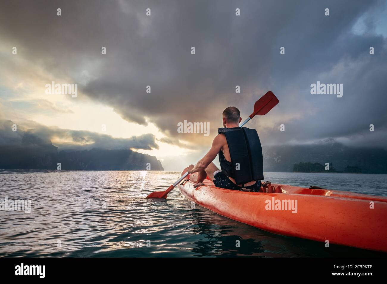 Uomo che galleggia in kayak al mattino sotto il cielo dell'alba sul lago Cheow LAN, Khao Sok National Park, Thailandia Foto Stock