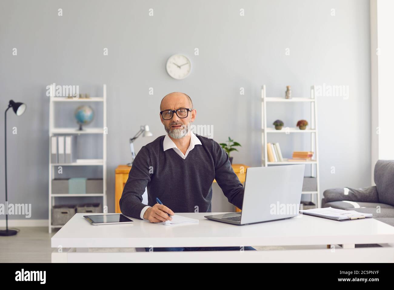 Uomo anziano serio che lavora online su netbook moderni a casa. Imprenditore che usa Internet per la conferenza di affari Foto Stock