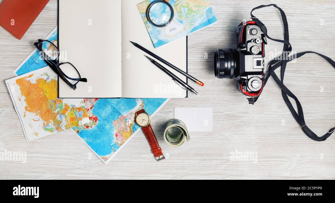 Piano di viaggio sfondo. Pronto per il viaggio. Mappa, notebook vuoto, macchina fotografica, occhiali, matite, orologio e denaro su tavolo di legno chiaro. Vista dall'alto. Disposizione piatta. Foto Stock