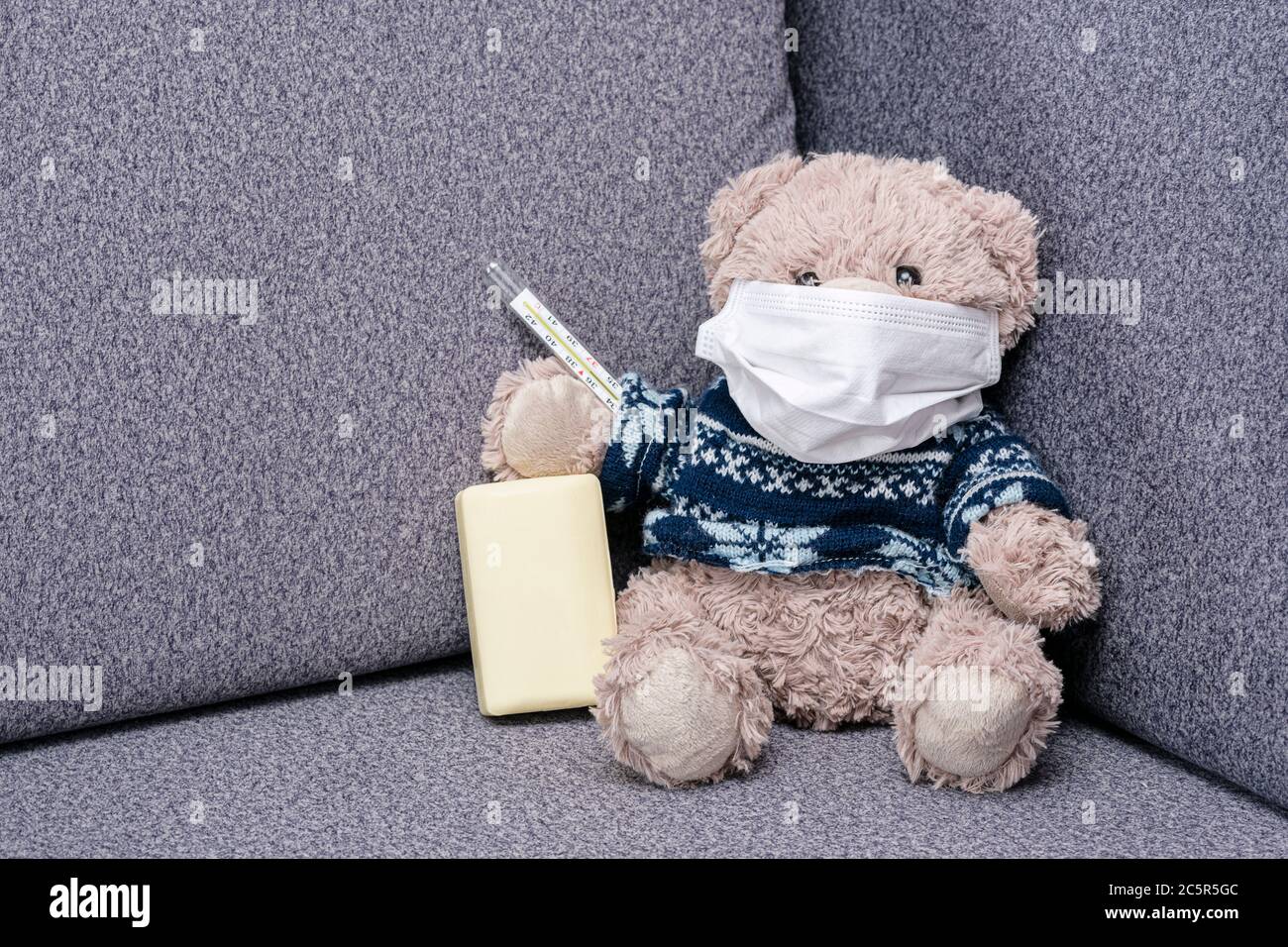 L'orso si siede sul divano in maschera medica protettiva. Maschera protettiva per la protezione contro il coronvirus e l'epidemia di influenza. Aiuto visivo per i bambini circa i mezzi di Foto Stock
