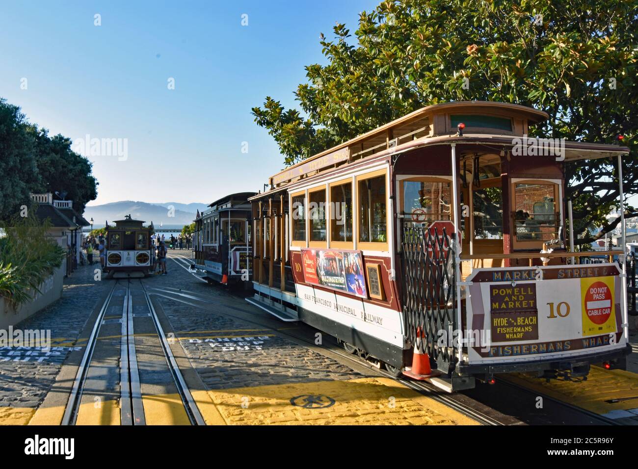 Powell e Hyde Line Cable Cars aspettano presso Hyde e Beach Turntable, colline attraverso la baia visibile in lontananza a San Francisco, California. Foto Stock