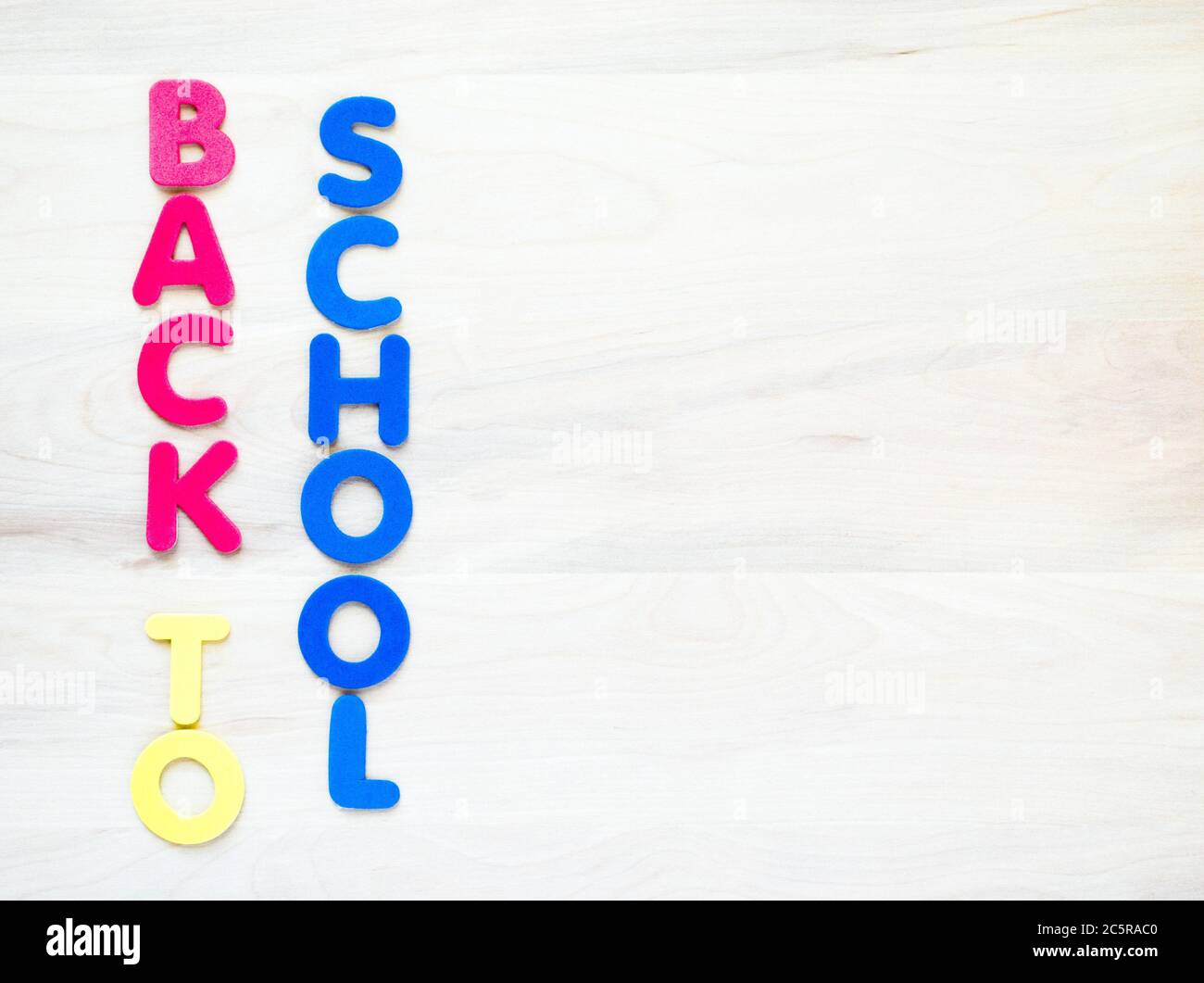 Lettere verticali in schiuma rossa, gialla e blu con la scritta "Torna a scuola" su sfondo di legno con spazio per la copia Foto Stock