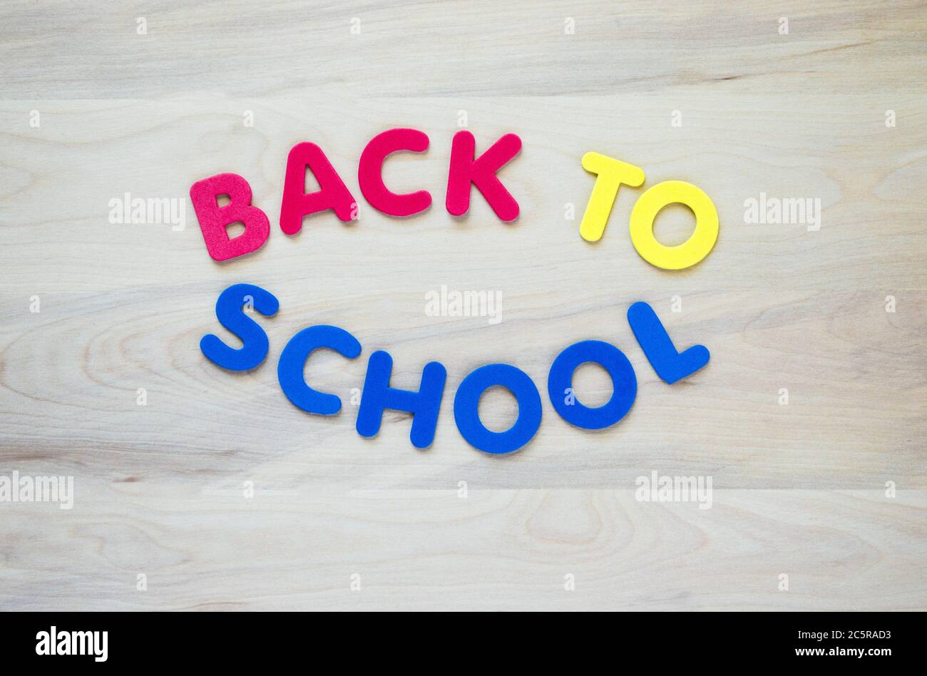 Lettere in schiuma rossa, gialla e blu con la scritta "Torna a scuola" su sfondo di legno con spazio per la copia Foto Stock