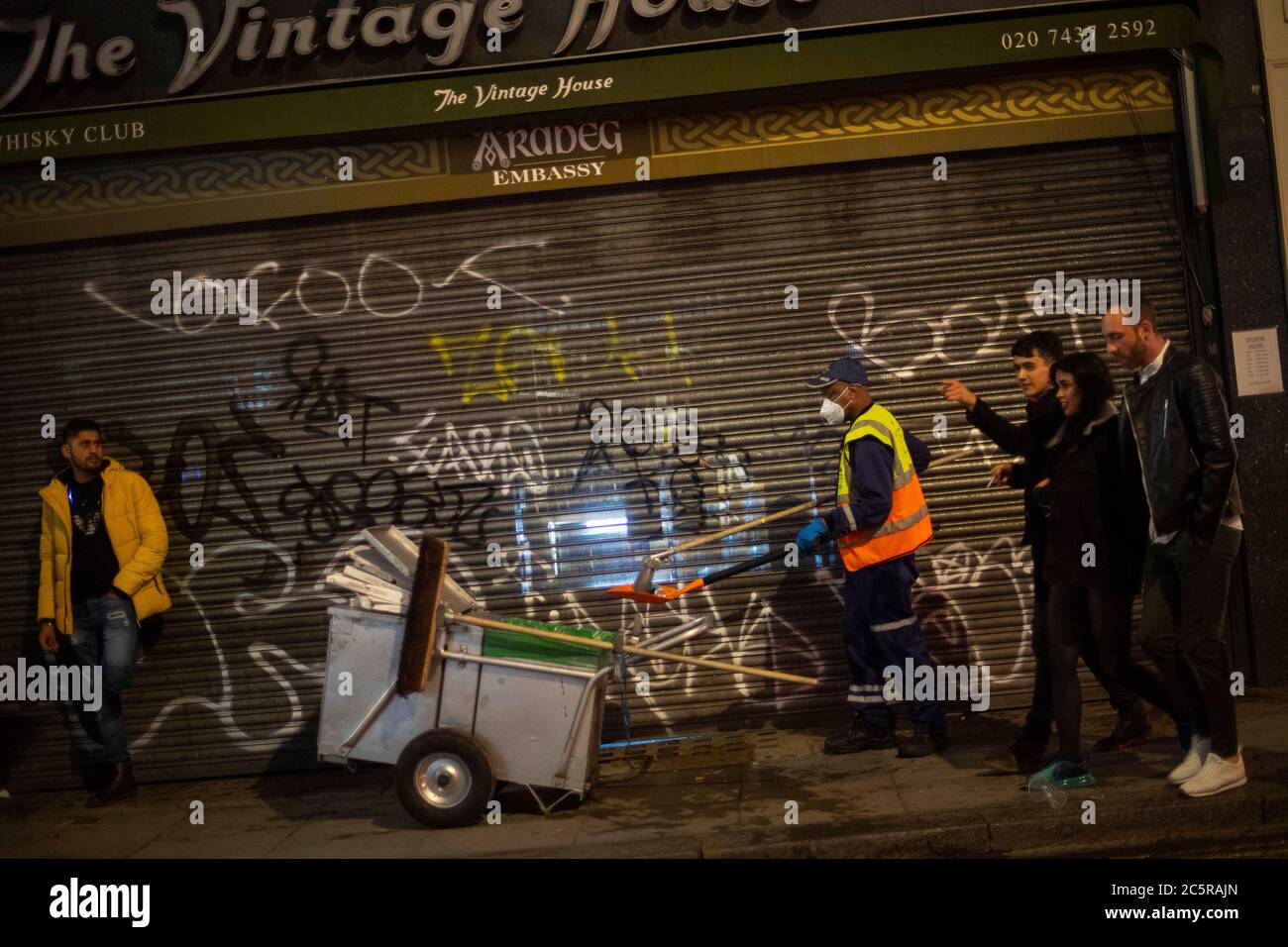 Un pulitore di strada passa in una strada a Soho, mentre i bevitori di tarda notte continuano nelle prime ore della domenica mattina, mentre le restrizioni di blocco del coronavirus sono attenuate in tutta l'Inghilterra. Foto Stock