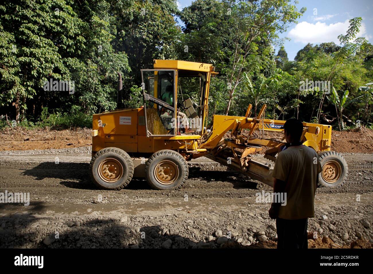 Un uomo che presta attenzione ad un veicolo di ingegneria in movimento come una nuova infrastruttura stradale è in fase di sviluppo in un'area remota all'interno della reggenza di Kapuas Hulu, provincia di Kalimantan occidentale, Indonesia. Foto di archivio (2012). Foto Stock