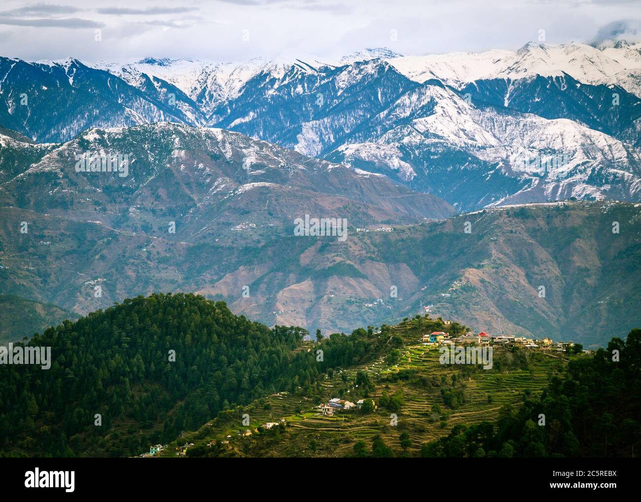 Un villaggio panoramico sullo sfondo delle montagne innevate dell'Himalaya in inverno. Himachal Pradesh, India. Foto Stock