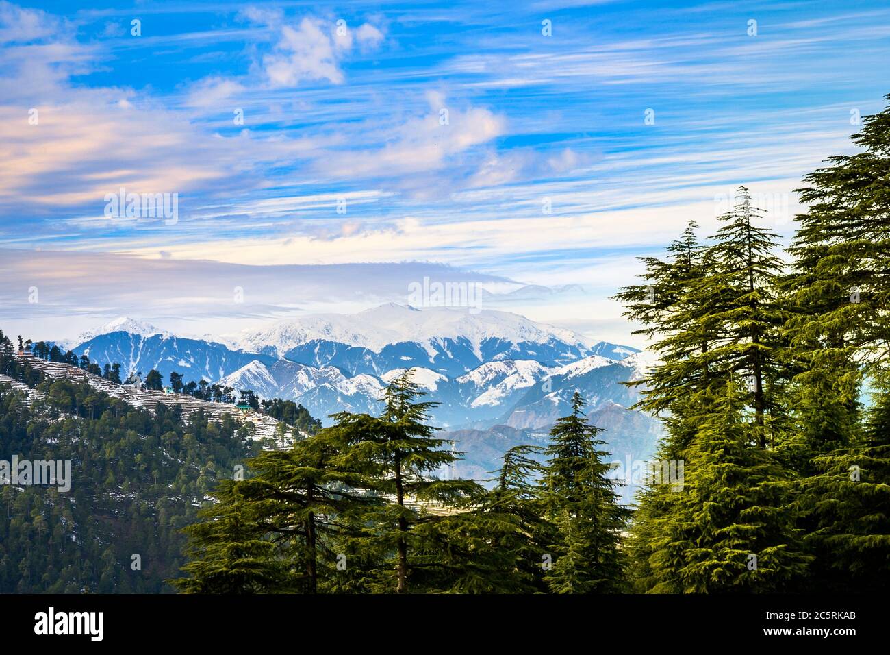 Un villaggio panoramico sullo sfondo delle montagne innevate dell'Himalaya in inverno. Himachal Pradesh, India. Foto Stock