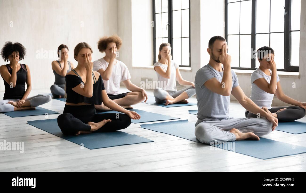 Motivata gente multirazziale focalizzata che pratica Nostril alternativo respirazione. Foto Stock