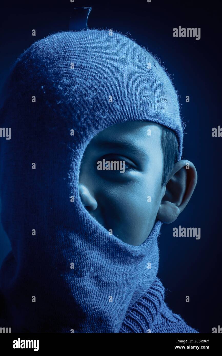 Studio ritratto di un ragazzo in una Balaclava blu, acceso l'orecchio sinistro. Tinta a freddo Foto Stock