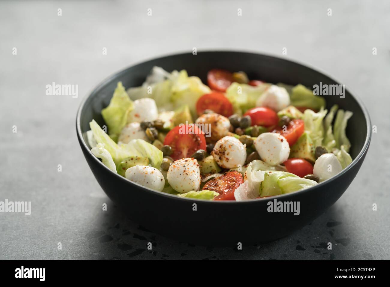 Insalata con avocado, pomodori e mozzarella in ciotola nera Foto Stock