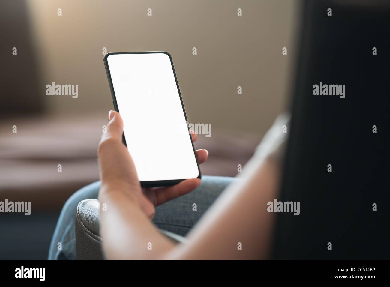 Giovane donna seduta in sedia con smartphone moderno con bianco schermo Foto Stock