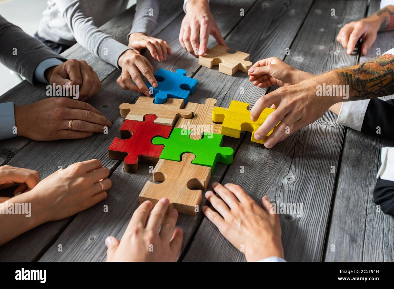 Il team di persone di affari seduti intorno al tavolo di riunione e l'assemblaggio di pezzi di puzzle a colori unità idee di cooperazione concetto Foto Stock