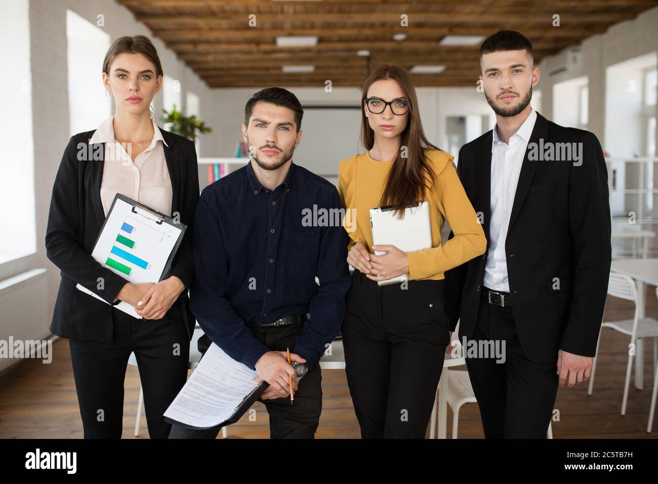 Gruppo di persone aziendali serie in tute che guardano con attenzione in macchina fotografica insieme mentre si passa il tempo al lavoro in un ufficio moderno Foto Stock