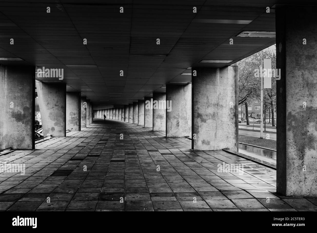 Lungo corridoio urbano curvo con pilastri in cemento e pavimentazione nella città di Rotterdam, Olanda, Paesi Bassi, cupo bianco e nero Foto Stock