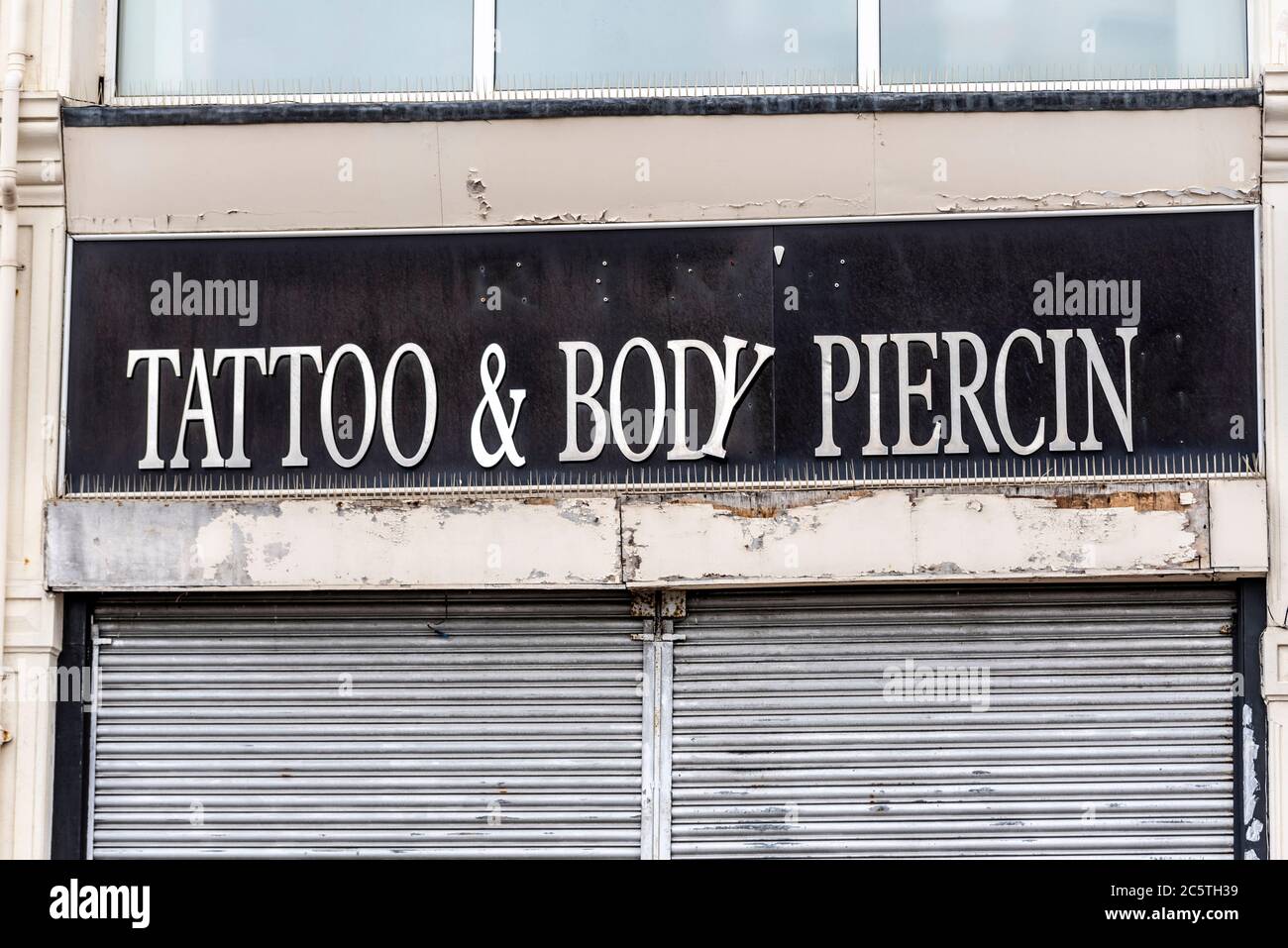 Negozio di tatuaggi e body piercing a Southend on Sea, Essex, Regno Unito. Locali chiusi e chiusi con lettere in decomposizione, danneggiate e lettera mancante Foto Stock