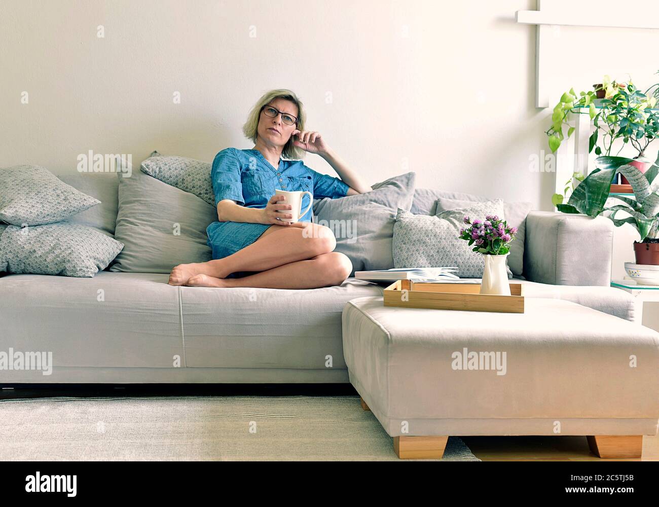 oltre 40 donne sedute su un divano grigio in un abito in denim e bevendo tè Foto Stock